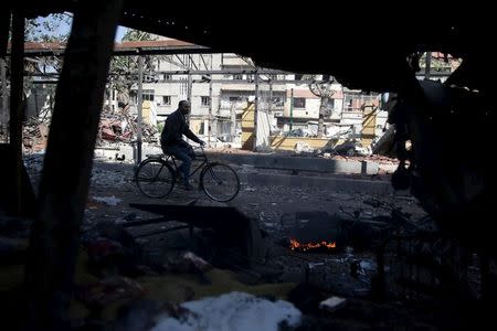 A man rides a bicycle at a damaged site hit by missiles fired by Syrian government forces on a busy marketplace in the Douma neighborhood of Damascus, Syria October 30, 2015. REUTERS/Bassam Khabieh