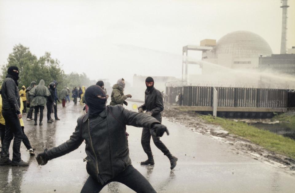 FILE - Demonstrators hurl rocks toward police water cannons behind the security fence surrounding the nuclear power plant in Brokdorf, West Germany, June 7, 1986. Germany is shutting down its last three nuclear power plants on Saturday, April 15, 2023, as part of an energy transition agreed by successive governments. The final countdown, delayed for several months over feared energy shortages because of the Ukraine war, is seen with relief by Germans who have campaigned against nuclear power. (AP Photo/Heribert Proepper, File)