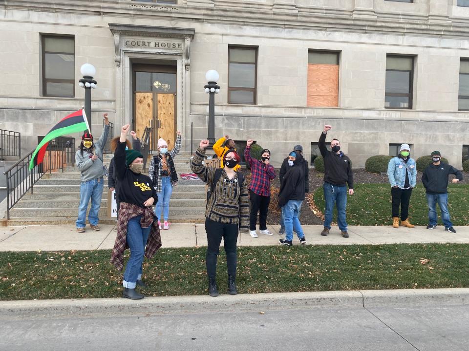 several people stand outside a court house wearing masks and raising their fists