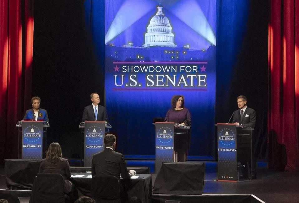 Four people stand at lecterns on a debate stage