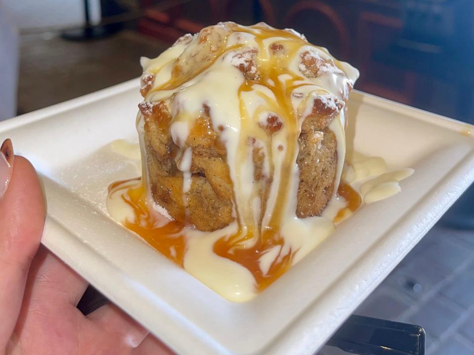 hand holding a gooey cinnamon roll with frosting and caramel from disney world