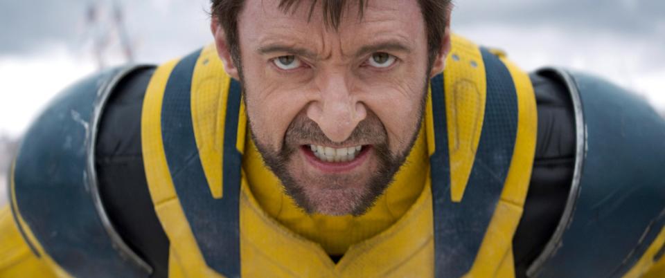 Hugh Jackman, wearing a futuristic yellow outfit, leans forward with a fierce expression, appearing ready for action