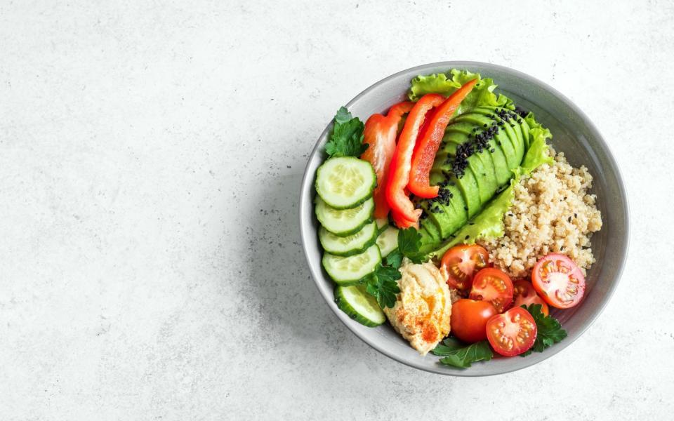 Healthy vegan lunch bowl, balanced eating buddha bowl. Avocado, quinoa, tomato, cucumber, hummus, bell pepper, seeds and greens vegetables salad, top - Oksana Bratanova / Alamy Stock Photo