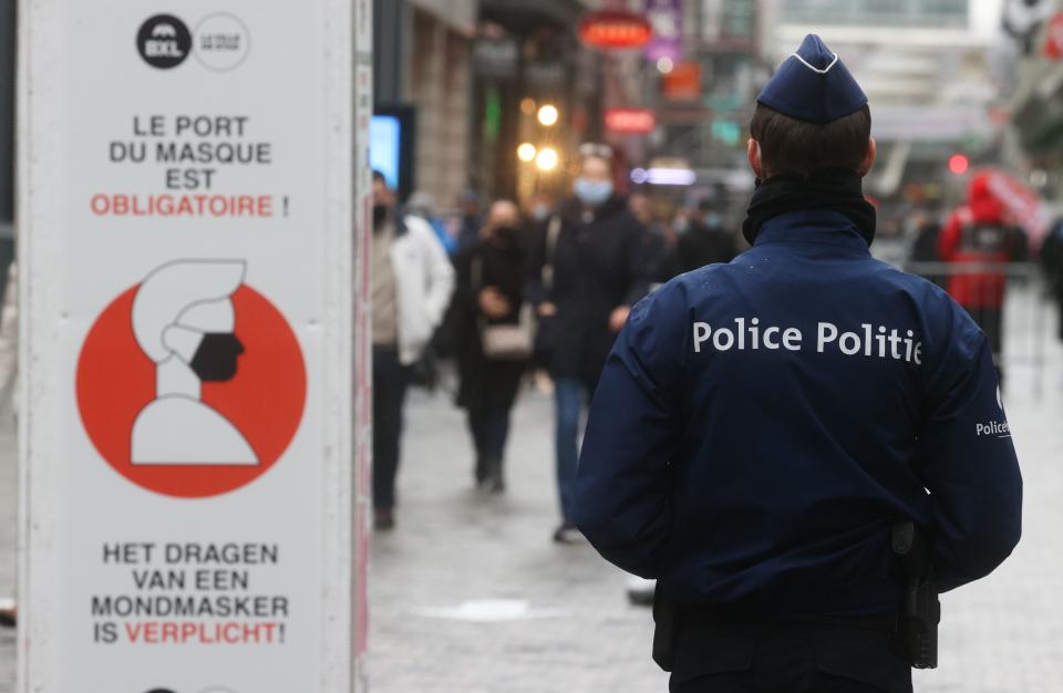 A policeman walks past a board asking to wear a face mask on December 1, 2020 in Brussels  as shops selling non-essentials goods are allowed to reopen under strict conditions amidst the new coronavirus pandemic.