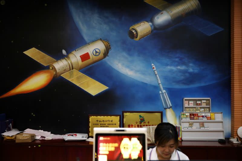 A hotel employee sits in front of a painting depicting a Chinese space mission in Wenchang, Hainan