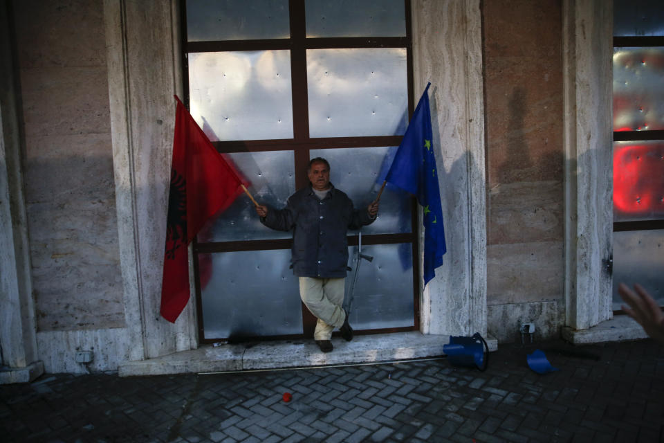 An opposition protester holding EU and Albanian flags stands at the entrance of the prime ministry during an anti-government rally in Tirana, Albania, Saturday, April 13, 2019. Albanian opposition parties have gathered supporters calling for the government's resignation and an early parliamentary election. (AP Photo/Visar Kryeziu)