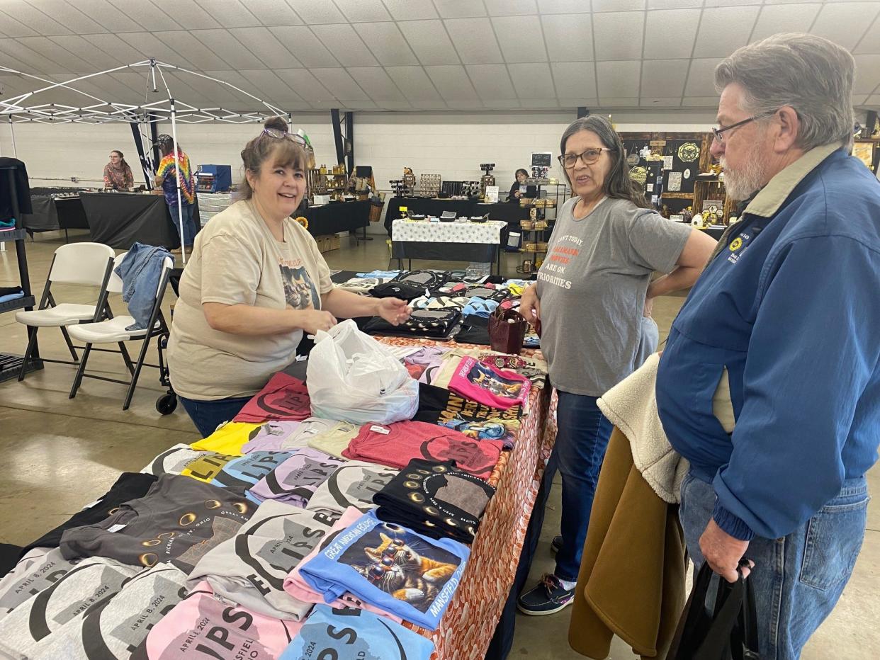Carla Wrasse, at left, works for her mother's business, American Graphics on Ashland Road, selling eclipse T-shirts to Sandy and Rick Montgomery of Mansfield Sunday from the Richland County Fairgrounds.