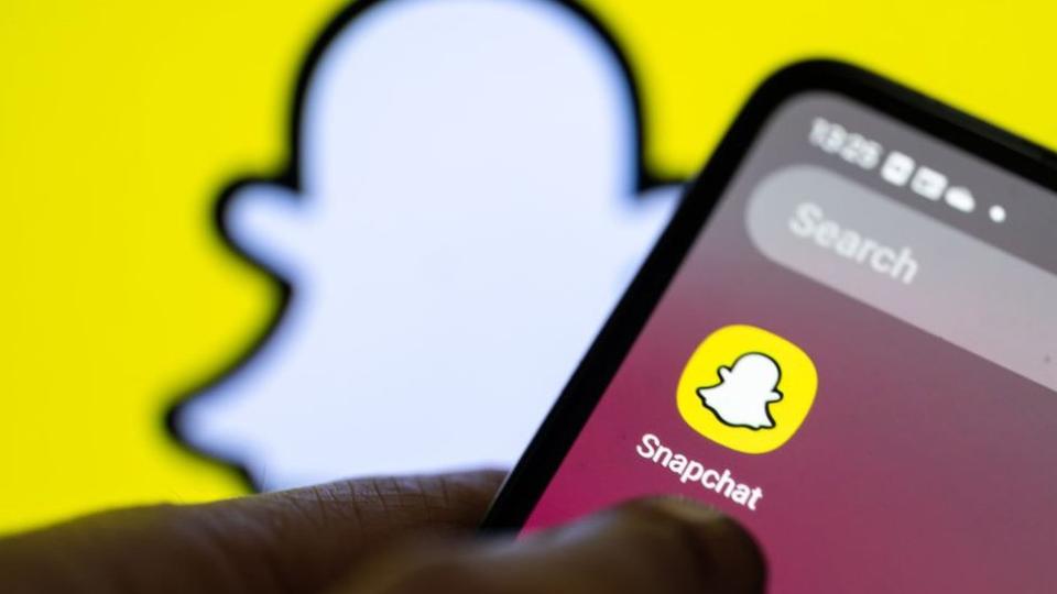 Stock image shows the Snapchat app on a smartphone against a backdrop of the the platform's logo