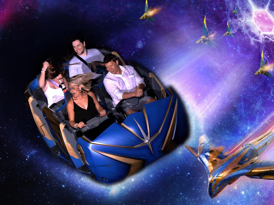 Terri Peters and her husband riding on the Guardians of the Galaxy ride. Her hair is in front of her face and her husband looks to the right, laughing. The photo is edited to make it look like they are flying through space with a bright hex shape on the right and battle spaceships approaching.