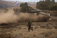 An Israeli soldier walks in front of a moving tank with an Israeli flag on the top in a staging area near the Israeli border with Lebanon, on Sunday, Oct. 15, 2023. (AP Photo/Petros Giannakouris)