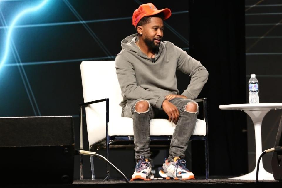 Zaytoven sitting onstage next to a small table with a bottle of water on top