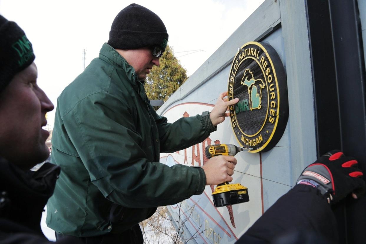 DNR Park rangers DJ Coffey (right) and Kale Leftwich add a DNR sign to the Belle Isle entrance sign on Monday February 10, 2014 during the first day the park in Detroit became a state park.
