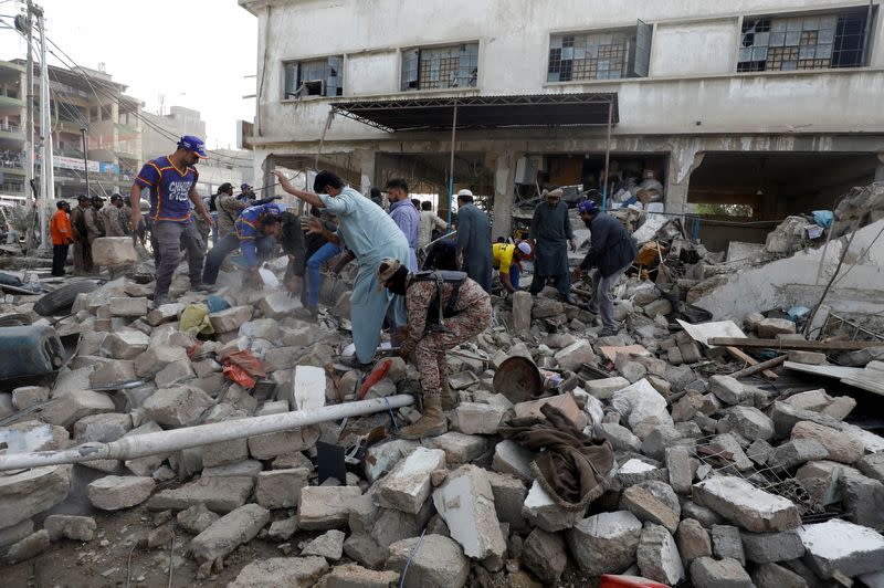 People and paramilitary personnel clear the rubble after a blast in an industrial area in Karachi
