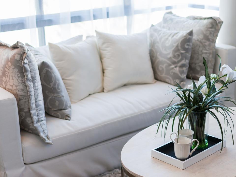 living room plant on table faux plant white couch stuffed with pillows too many pillows