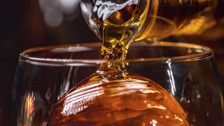 Close-up of whiskey pouring into a glass with a large ice ball