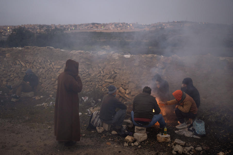 Palestinian labourers warm themselves around a fire as they wait for transportation after crossing a checkpoint from the West Bank city of Bethlehem into Jerusalem, March 15, 2022. For more than two years, the Biden administration has said that Palestinians are entitled to the same measure of “freedom, security and prosperity” enjoyed by Israelis. Instead, they've gotten U.S. aid and permits to work inside Israel and its Jewish settlements. The inconsistency is likely to come up when President Joe Biden visits Israel and the occupied West Bank this week for the first time since assuming office. (AP Photo/Oded Balilty)