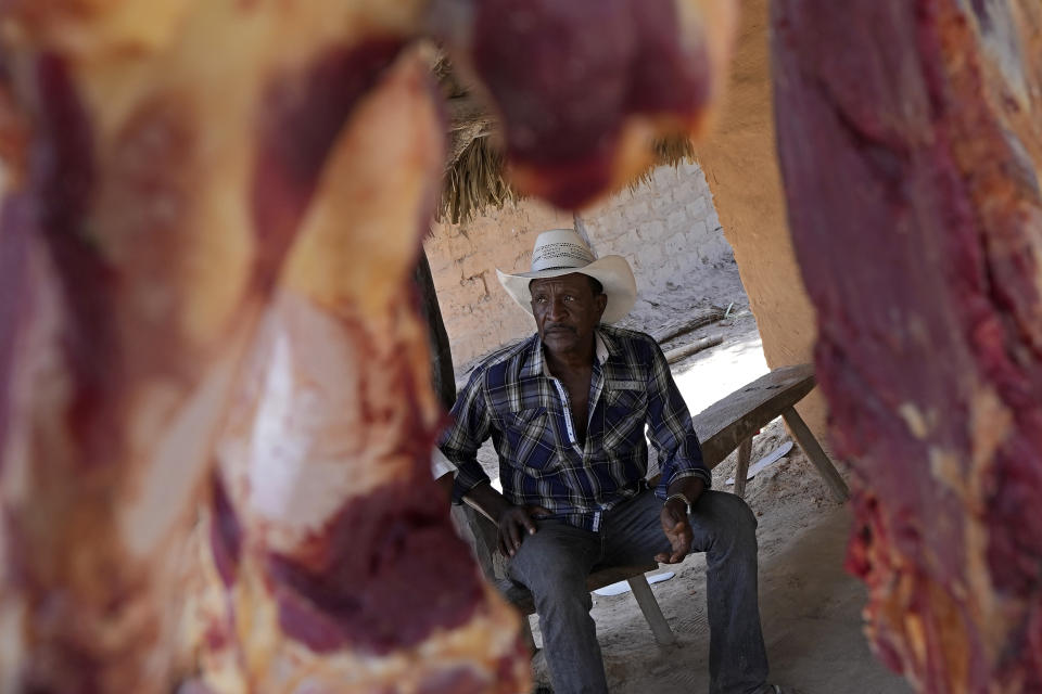 A member of the Kalunga quilombo, the descendants of runaway slaves, is framed between racks of beef offered for sale during the culmination of the week-long pilgrimage and celebration for the patron saint "Nossa Senhora da Abadia" or Our Lady of Abadia, in the rural area of Cavalcante in Goias state, Brazil, Saturday, Aug. 13, 2022. Devotees celebrate Our Lady of Abadia at this time of the year with weddings, baptisms and by crowning distinguished community members, as they maintain cultural practices originating from Africa that mix with Catholic traditions. (AP Photo/Eraldo Peres)