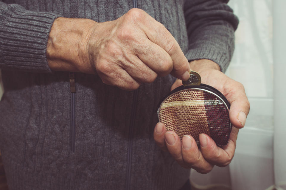 An elderly man puts a coin in an empty wallet. Poverty in retirement concept. Special toning