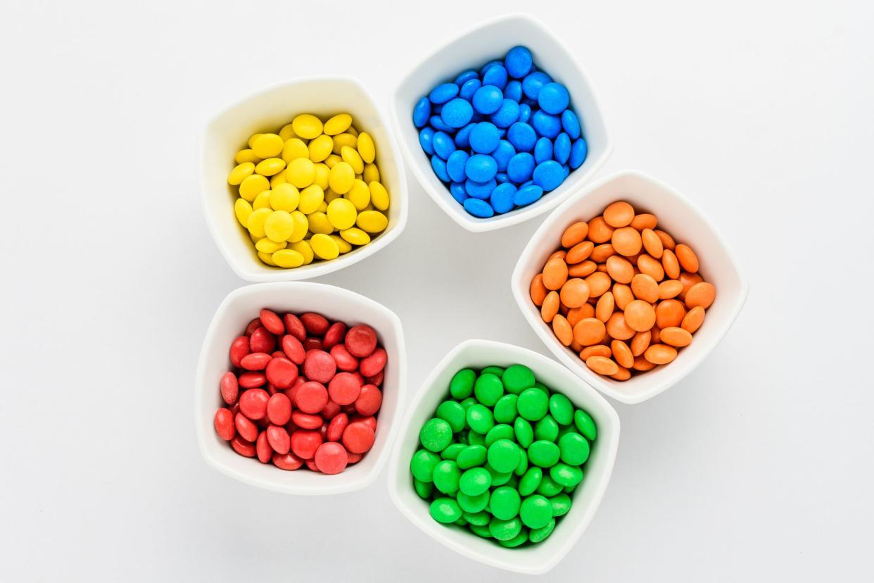 Five squared bowls with small red, yellow, blue, green and orange coated chocolate candies similar to m&ms in a squared bowl isolated on white background, top view