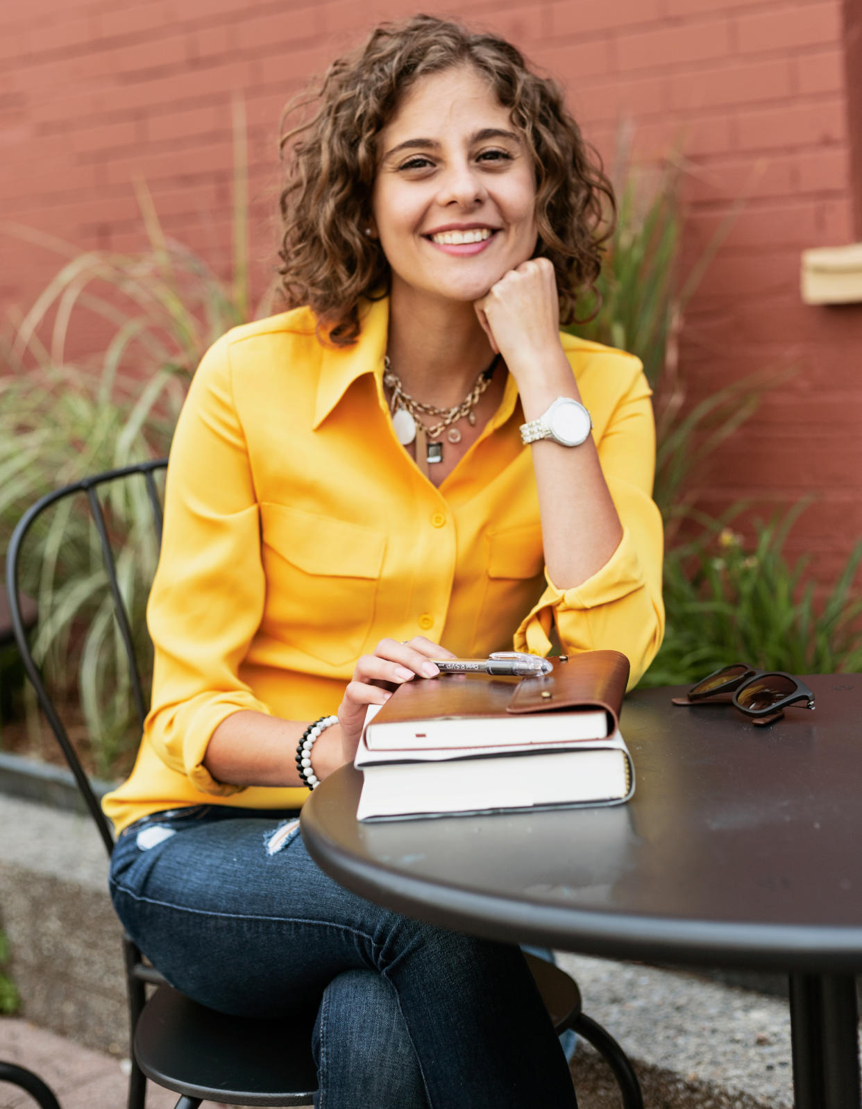 Woman sitting and smiling in a yellow top in front of books on a table