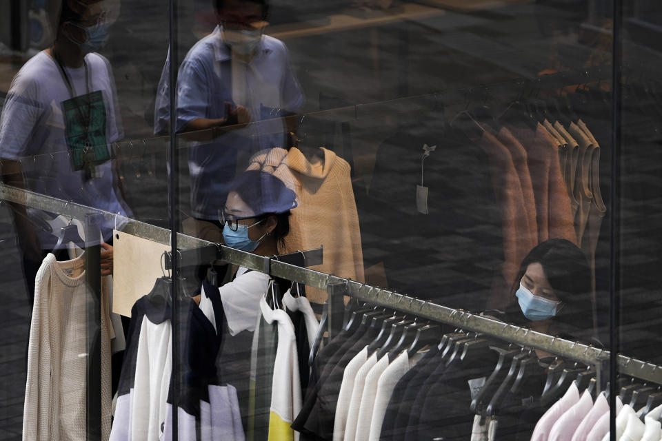 People wearing face masks to help protect from the coronavirus walk through a capital popular shopping mall as masked women selecting clothes at a fashion boutique in Beijing, Tuesday, Sept. 28, 2021. The World Bank on Tuesday cut its economic growth forecast for developing countries in East Asia due to the impact of the coronavirus's delta variant and called on governments to help the poor and small businesses avoid long-term damage. (AP Photo/Andy Wong)