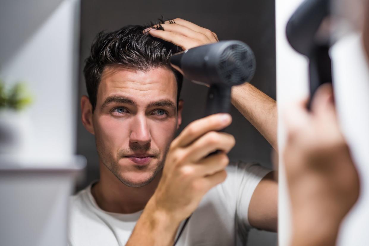 Man using hair dryer while looking himself in the mirror.