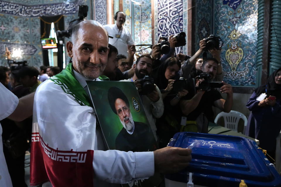 Un hombre vota en las elecciones presidenciales anticipadas en Irán mientras sostiene una foto del difunto presidente Ebrahim Raisi, en un centro de votación en Teherán, Irán, el 28 de junio de 2024. (AP Foto/Vahid Salemi)