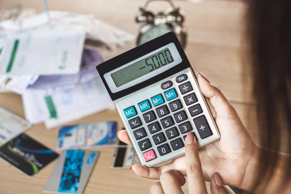 woman hand holding calculator showing number budget deficit for credit card debt payment with some bills on desk