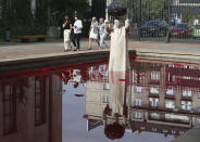 Visitors to the National Museum walk past a new statue of the late pope, St. John Paul II, throwing a stone at a "Poisoned Well" just hours before its official inauguration in the museum yard in Warsaw, Poland, Thursday, Sept. 24, 2020. The sculpture by Poland's Jerzy Kalina is said to be a response to a controversial 1999 sculpture by Italian Maurizio Cattelan in which the Polish-born pontiff was shown as being crushed by a similar stone. (AP Photo/Czarek Sokolowski)