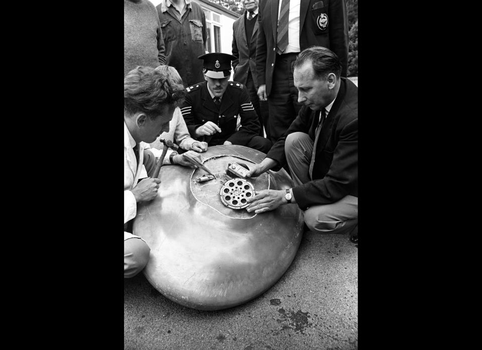 Engineer Reg Willard (left) chips away with a chisel as he dissects the bleep mechansim of the mystery object found at Clevedon, Somerset, by a schoolboy. Helping him is Aubrey Willcocks, who was called in by the local police. Looking on is Sergeant John Durston. The object was one of five strange objects, all resembling flying saucers and emitting noises, found in different parts of the country. Inside the object Mr Willard found two Exide batteries, a British made transmitter and a loudspeaker. (Photo credit: PA)