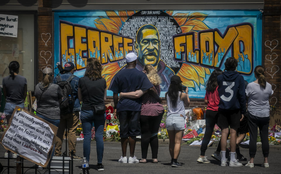 FILE - In this May 31, 2020 file photo, visitors make silent visits to organic memorial featuring a mural of George Floyd, near the spot where he died while in police custody, in Minneapolis, Minn. On Wednesday, Dec. 8, 2020, the Minneapolis City Council will decide whether to shrink the city's police department while violent crime is already soaring and redirect funding toward alternatives for reducing violence. (AP Photo/Bebeto Matthews, File)