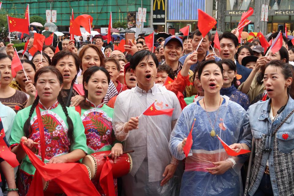 El bailarín Huang Doudou (C, primera fila) con una bandera nacional china canta con otros artistas durante un flash mob que celebra el 70 aniversario de la liberación de Shanghai en Century Square el 26 de mayo de 2019 en Shanghai, China. China marca el 70 aniversario de la liberación de Shanghai el 27 de mayo de 2019. Foto de VCG a través de Getty Images.