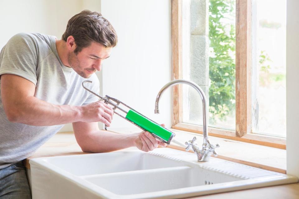 Man caulking around an enamel kitchen sink basin