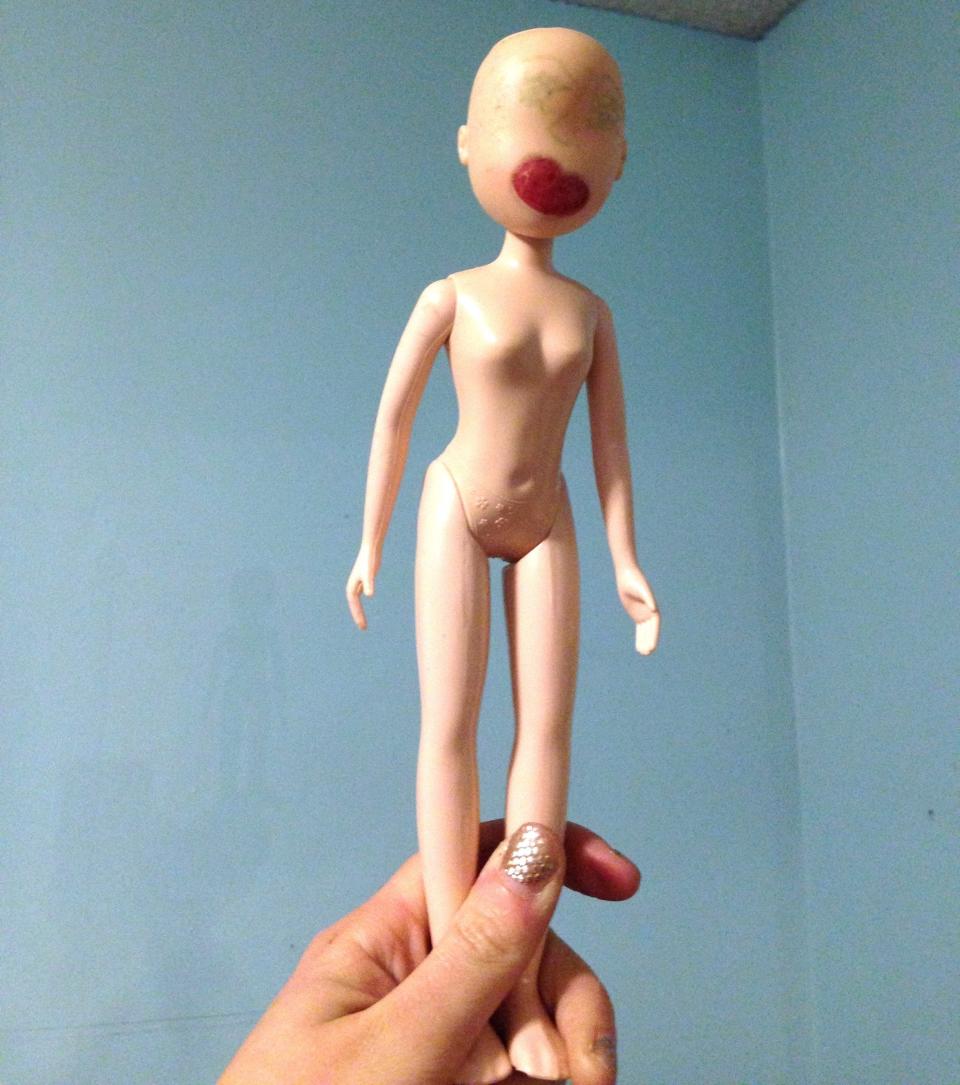 hand holding up a doll with only lips, no hair left