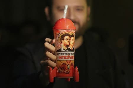 A man holds up a "The Interview" souvenir cup at the Silent Movie Theatre before a midnight screening of "The Interview" in Los Angeles, California December 25, 2014. REUTERS/Jonathan Alcorn