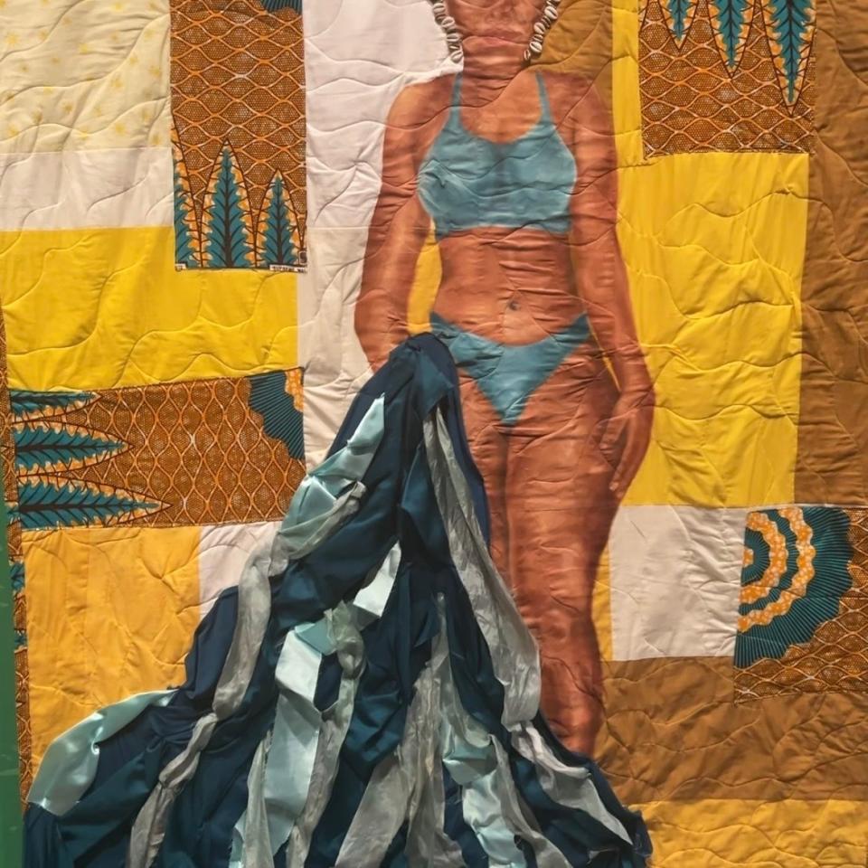 Art installation of a woman's portrait on a quilt with cascading fabric at the bottom, displayed in a gallery