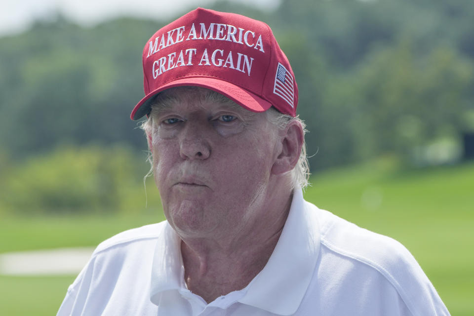 Former President Donald Trump, wearing a Make America Great Again hat, watches a tournament at a golf course.