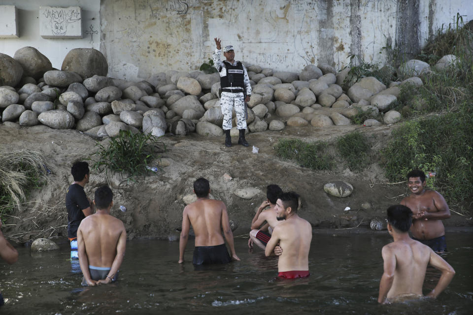 A Mexican National Guard speaks with Honduran migrants who wanted to cross into Mexico but returned to Guatemala as the migrants stand in the Suchiate River which separates Mexico from Guatemala near Ciudad Hidalgo, Mexico, Monday, Jan. 20, 2020. More than a thousand Central American migrants hoping to reach the United States marooned in Guatemala were preparing to walk en masse across a bridge leading to Mexico in an attempt to convince authorities there to allow them passage through the country. (AP Photo/Marco Ugarte)