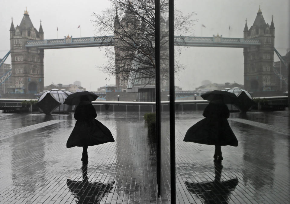 FILE - In this Thursday, Jan. 14, 2021 file photo a woman is reflected in a window as she braves wind and rain while walking towards Tower Bridge in London during England's third national lockdown to curb the spread of coronavirus. (AP Photo/Kirsty Wigglesworth, File)