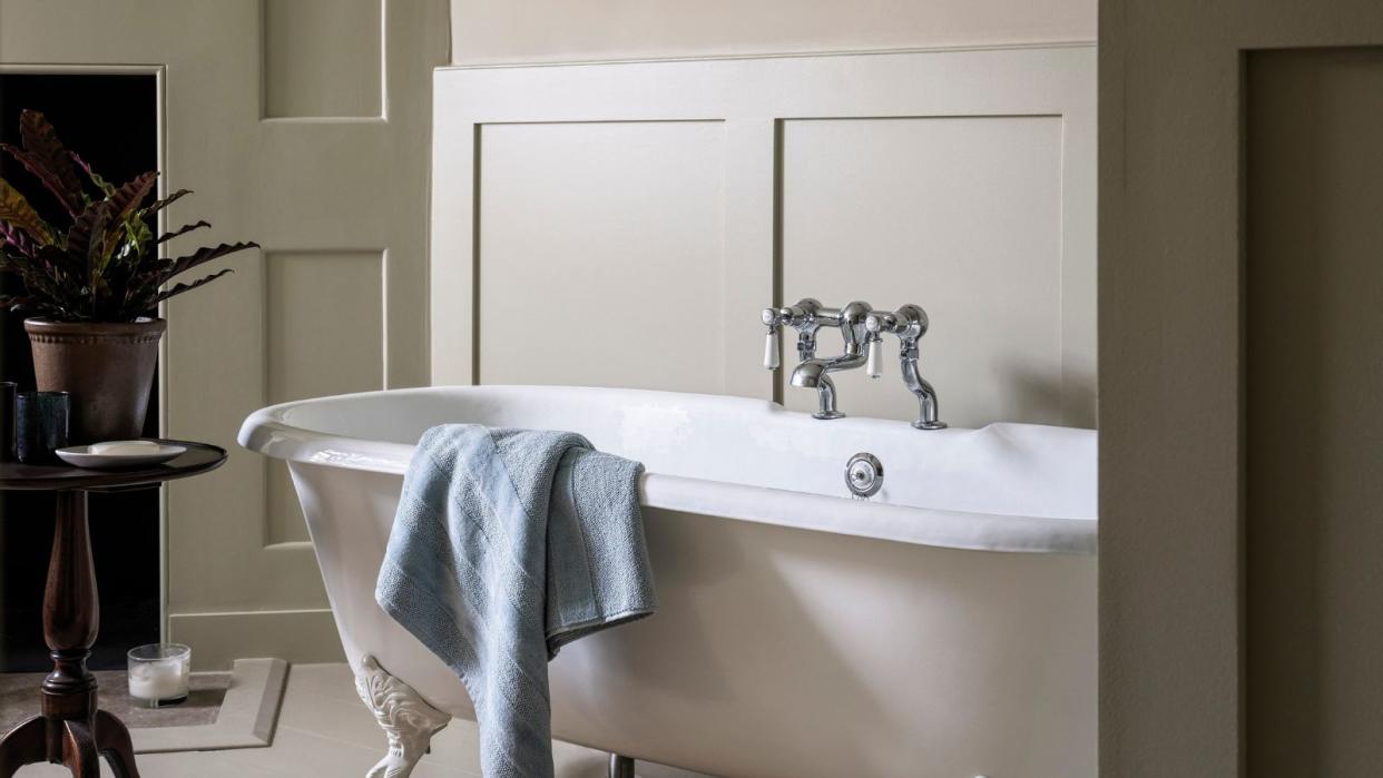  A cream roll top bath with a towel draped over the side and a small side tabel with essentials 