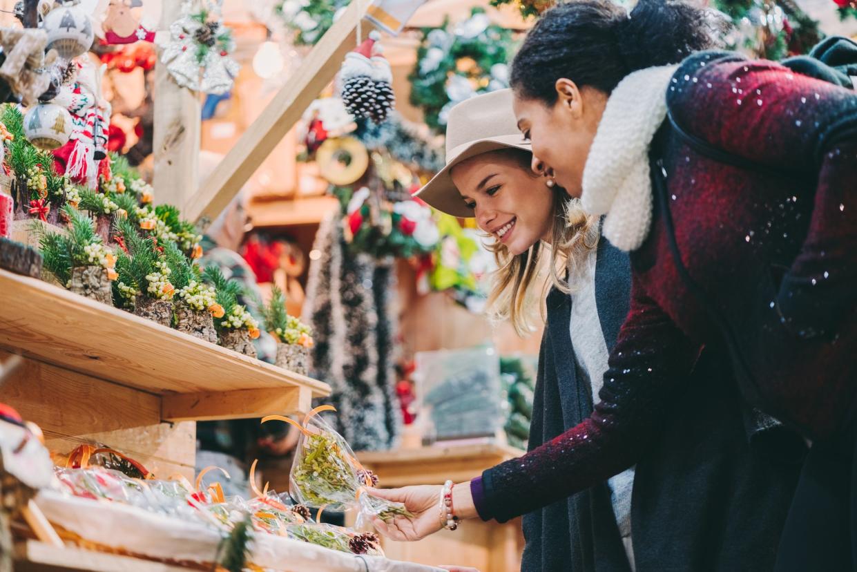 Side-view of two female friends choosing ornaments at a vendor in the Christmas market in Barcelona, with other vendors blurred in the background