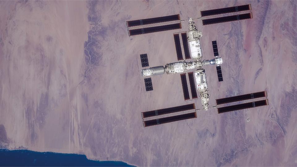 a large T-shaped space station is seen from above with Earth below it