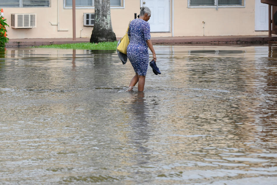 A woman carrying her shoes walks barefoot through a flooded street in Miami. 