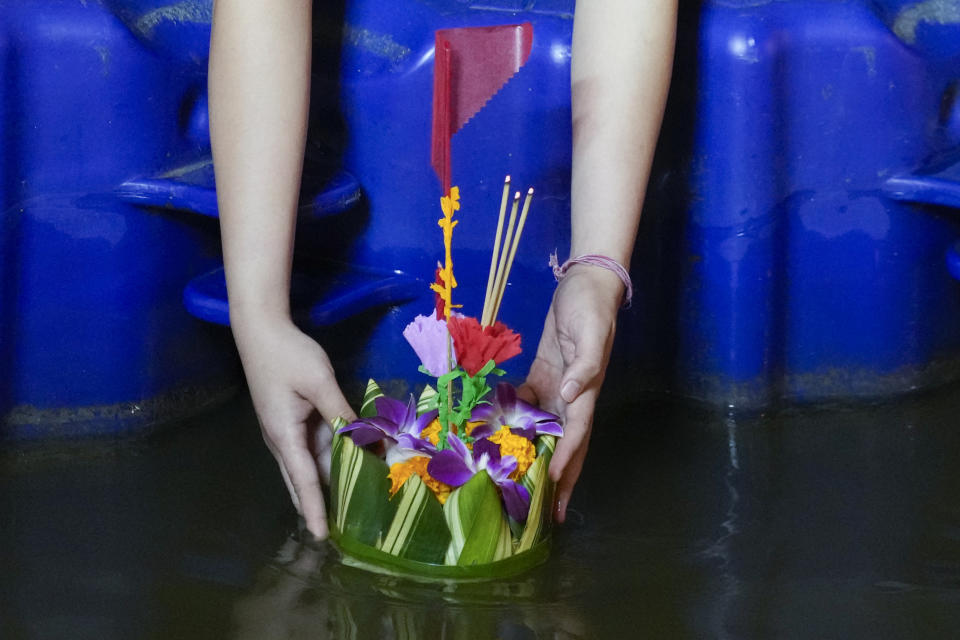 A Thai woman places a krathong, a small boat made of banana tree and decorated with banana leaves and flowers, into a Ong Ang canal during Loy Krathong festival in Bangkok, Thailand, Friday, Nov. 19, 2021. Thais believe that the candle-lit boats launched during the charming and popular Loy Krathong festival can carry the year's misfortunes away with them, but workers must clean up the waterways afterward to keep them from getting clogged and polluted. (AP Photo/Sakchai Lalit)