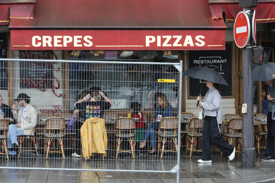 Patrons sit outside a restaurant behind a remaining security barrier on a street along the Seine River, now opened to foot traffic after Friday's opening ceremony, at the 2024 Summer Olympics, Saturday, July 27, 2024, in Paris, France. (AP Photo/Rebecca Blackwell)