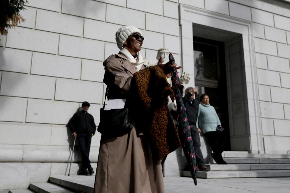 A woman in a coat smiles and applauds.