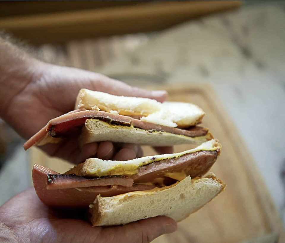 A person holds a sandwich with eggs and ham, cut diagonally, over a wooden board