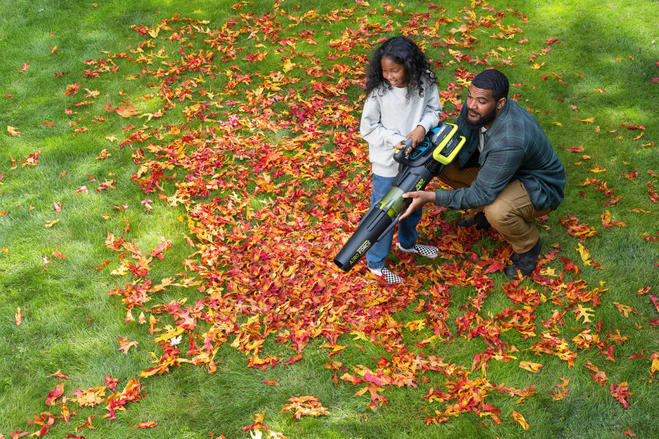 Man showing daughter how to use his Yardworks 48V Brushless AeroForce Leaf Blower from Canadian Tire to clean up leaves on the lawn