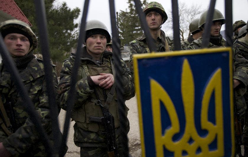 FILE - In this Sunday, March 2, 2014 file photo, Ukrainian soldiers guard a gate to their military base in the village of Perevalne, outside Simferopol, Ukraine. On the eve of a referendum vote that has the Black Sea peninsula resting on a razor’s edge, those facing the greatest and most fraught uncertainty was are Ukraine’s military forces on the peninsula, who have been hemmed in by heavily armed Russian troops and warned by the region’s pro-Russian leader that they would be considered “illegal” if they didn’t surrender. (AP Photo/Ivan Sekretarev, File)