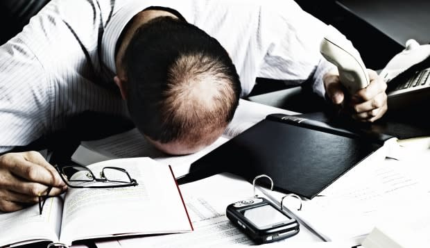 Totally desperate businessman with head on office desk top being overloaded with loads of work